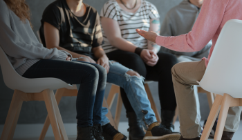 A group of five young people people sit in semi-circle as part of a therapy session. Their heads are not in the frame.