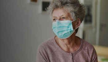 A senior citizen sits alone with a surgical mask