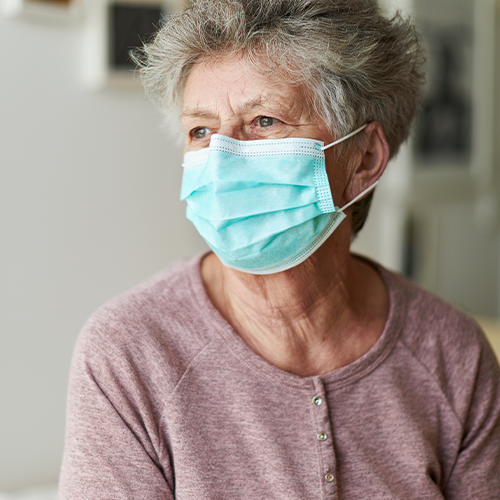 Stock image: a senior citizen sits alone on her bed with a respirator or surgical mask stock