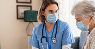 senior woman in facemask consults with nurse who is wearing a facemask