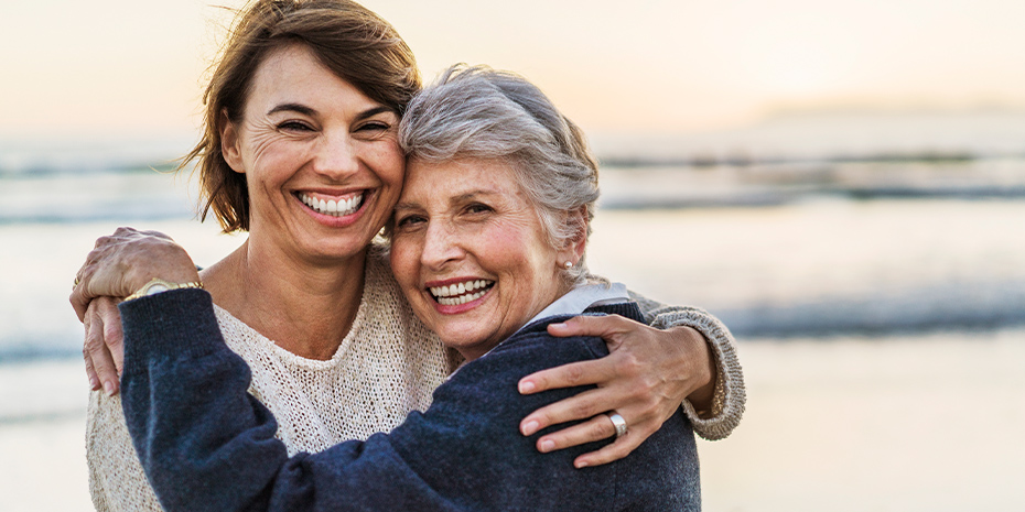 a senior mother hugging her adult daughter on the beach stock image