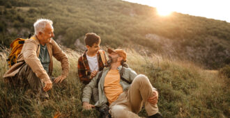 Elderly father with adult son and grandson relaxing in nature during hiking tour