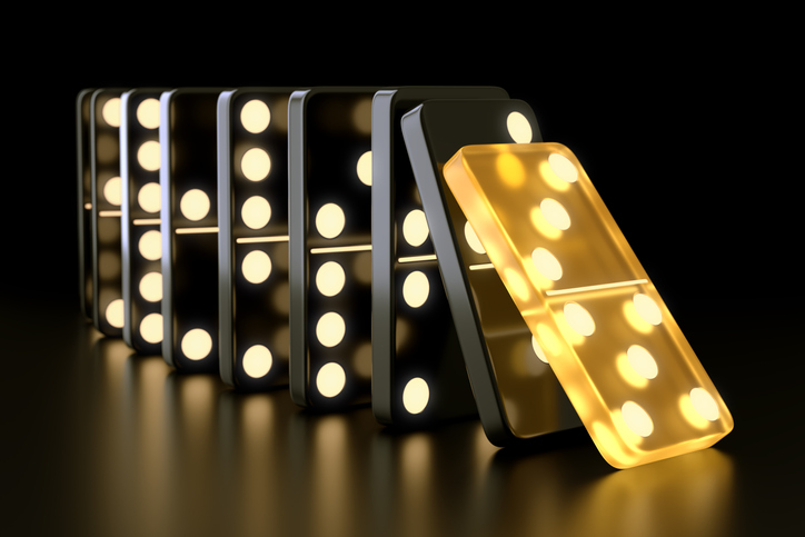 Unique glowing yellow domino tile falling on black dominoes on dark background.
