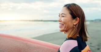 Asian woman holding surfboard on beach