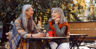 Mature Asian lady with positive grey-haired friend spend time together in street cafe