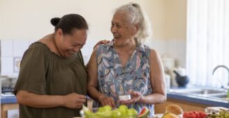 Senior woman laughing in the kitchen with daughter as they prepare healthy food.