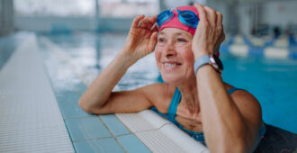 A happy senior woman in swimming pool, leaning on edge.